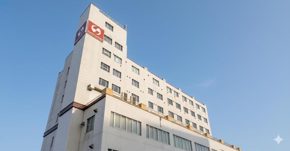 A multi-story building with a prominent red logo on the side, large windows, and a flat roof. - New Grand Hotel Shinjo (Shinjo)