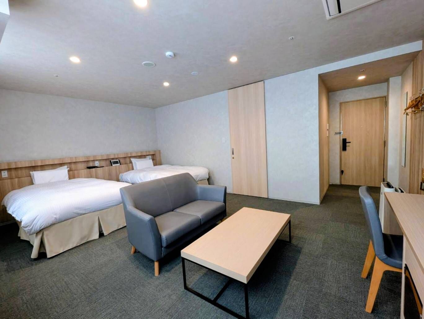 A hotel room with two beds, a sofa, a table, and a desk.