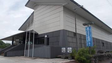 Um edifício moderno com telhado inclinado, uma escadaria que leva à entrada e uma placa azul com texto em japonês.