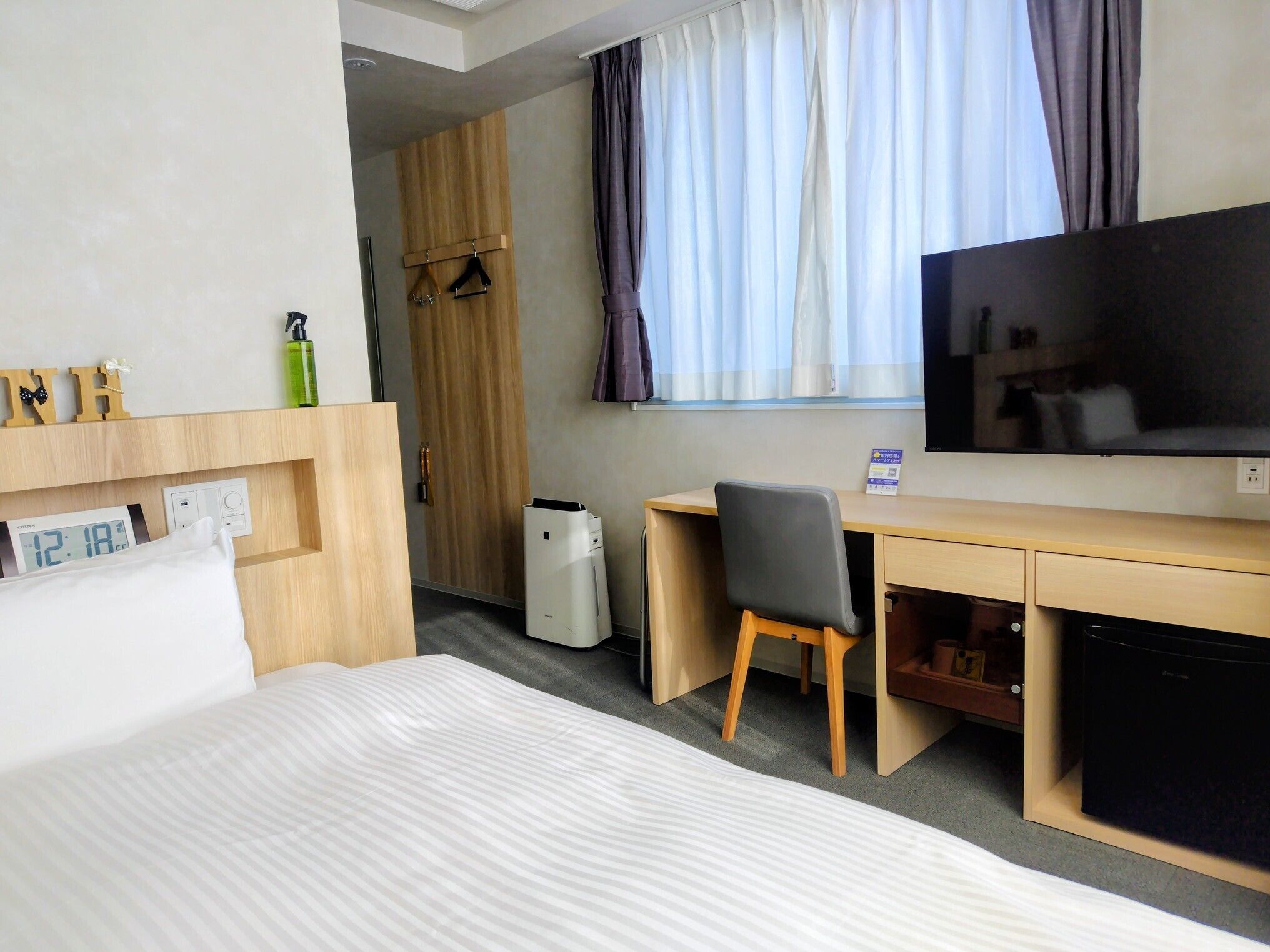 A hotel room with a bed, a desk, a chair, a TV, a wardrobe, and a window with curtains.