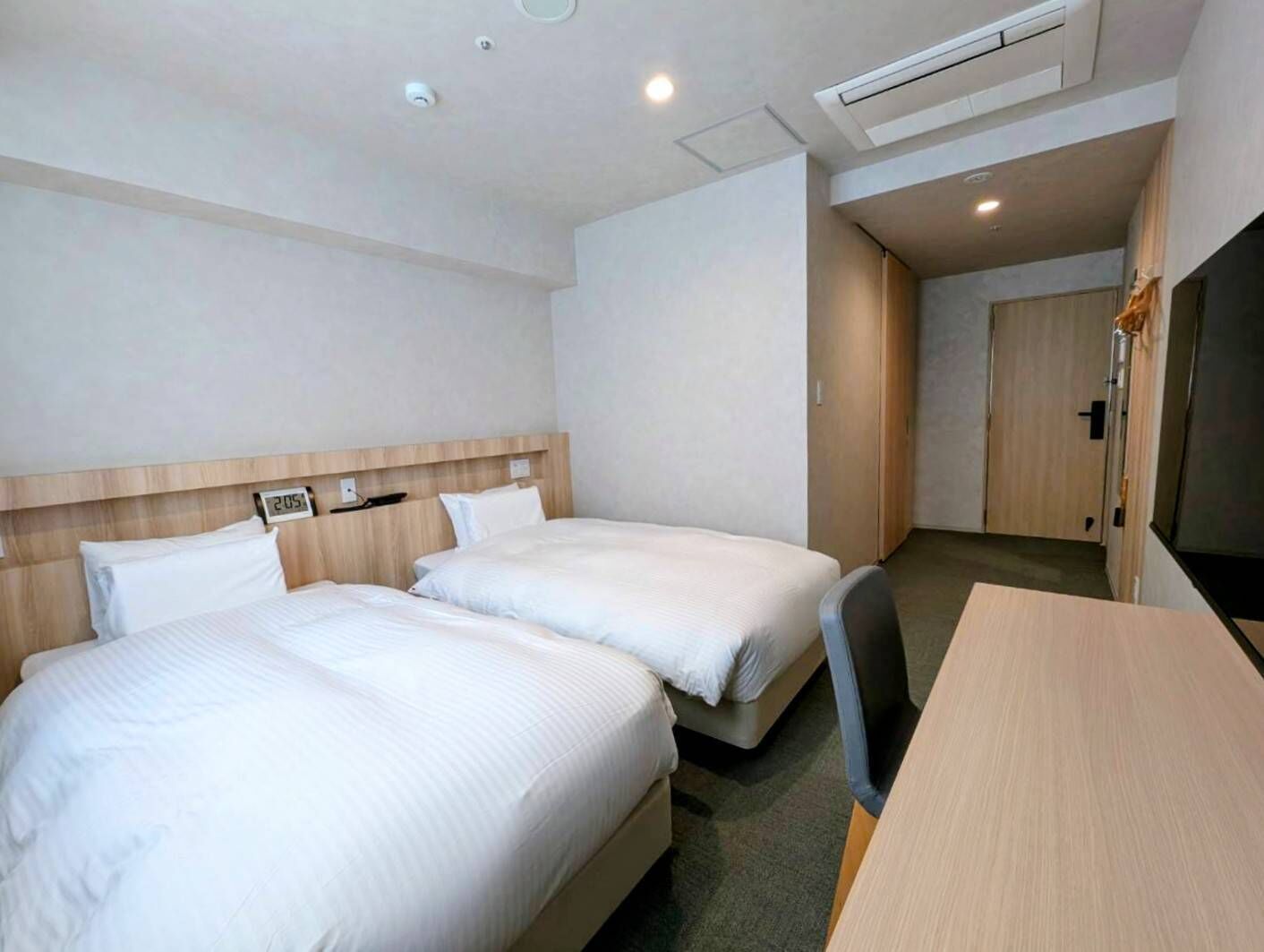 A hotel room with two beds, a desk, and a wardrobe.