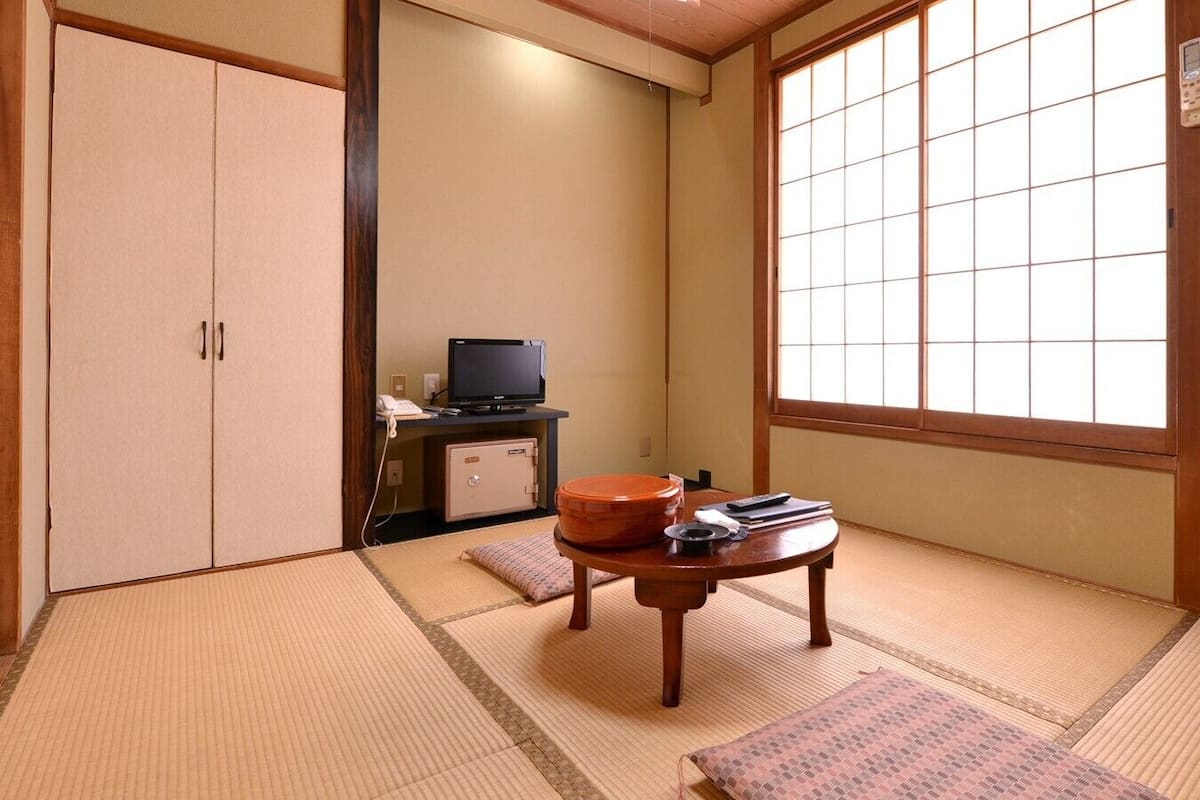 A traditional Japanese room with tatami flooring, a sliding door, a television, and a small table with items on it.