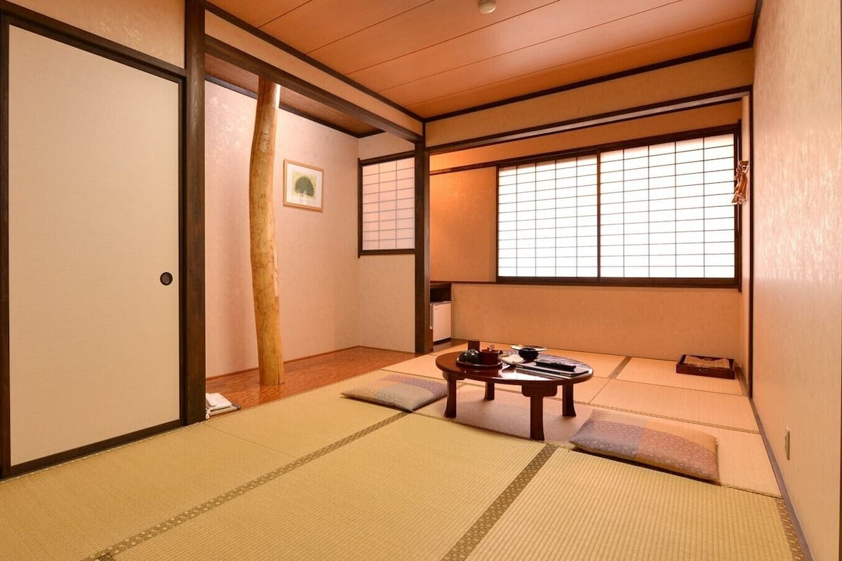 A traditional Japanese room with tatami flooring, a low table with tea set, sliding doors, and a window with shoji screens.