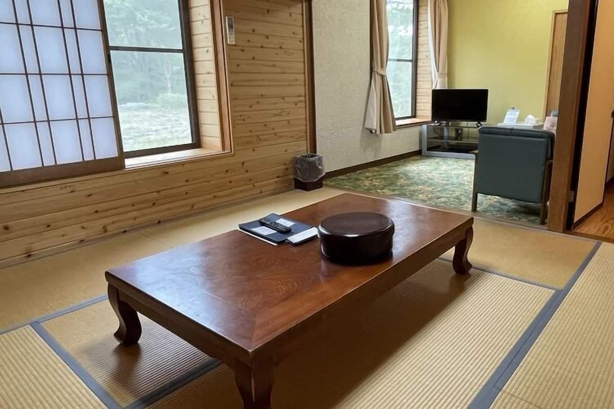 A traditional tatami mat room with a wooden table, a black round object, and a television in the background.