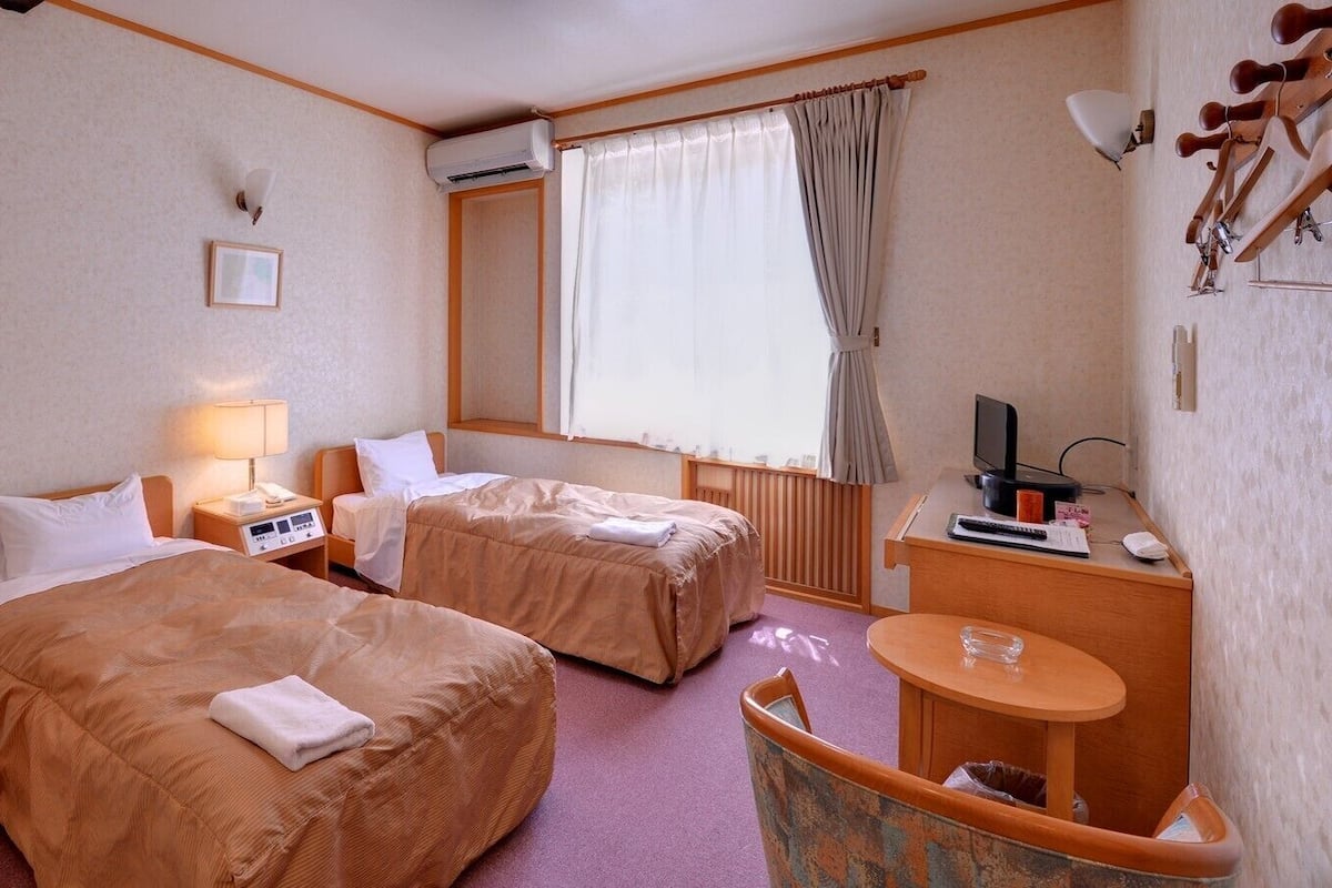 A hotel room with two beds, a desk with a computer, a TV, and a window with curtains.