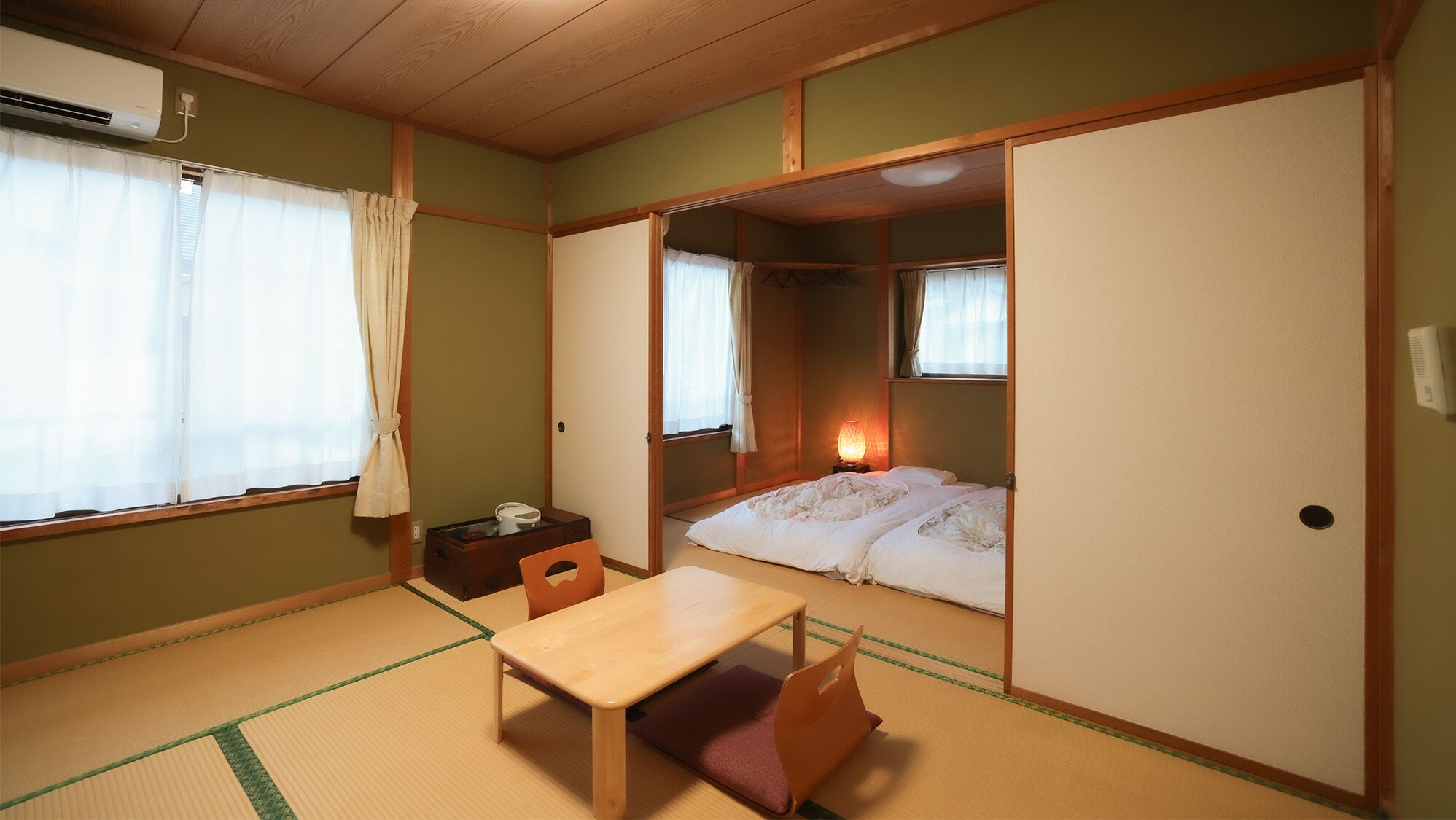 Une pièce de style japonais traditionnel, avec un sol recouvert de tatamis, un futon servant de lit, une petite table en bois et des portes coulissantes.