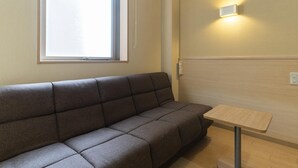 A room with a sofa, a small table, a window, and a wall-mounted light fixture. - Hotel Monzen No Yu (Joetsu)