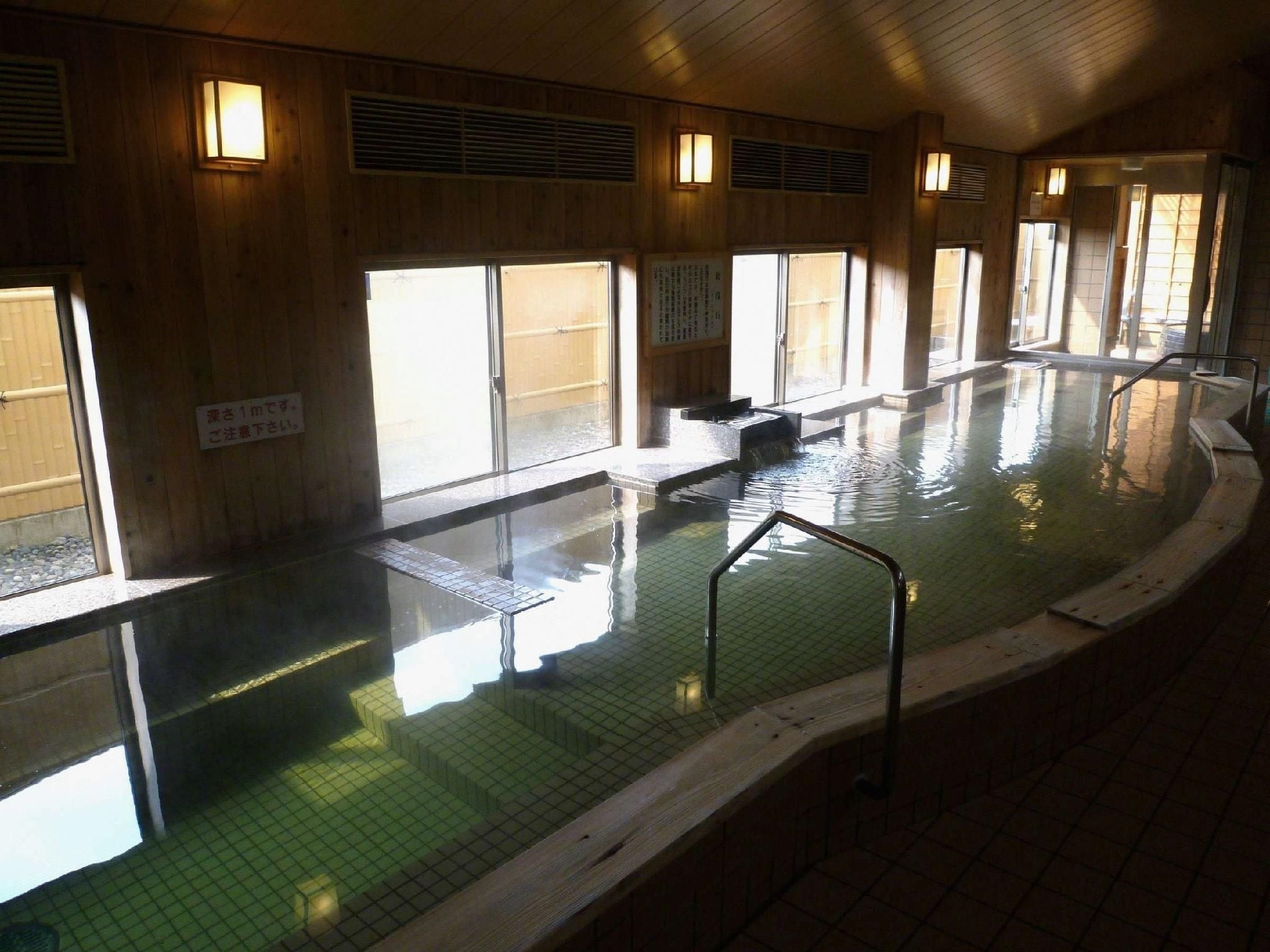 An indoor swimming pool with tiled walls and a wooden floor, surrounded by windows.