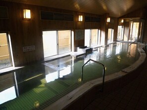 An indoor swimming pool with tiled walls and a wooden floor, surrounded by windows. - Hotel Monzen No Yu (Joetsu)