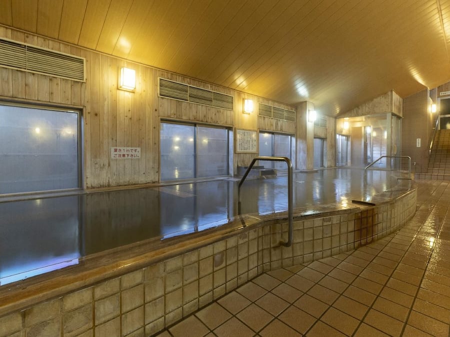 Un baño público con paredes de madera, suelo de baldosas y zona de piscina con azulejos.