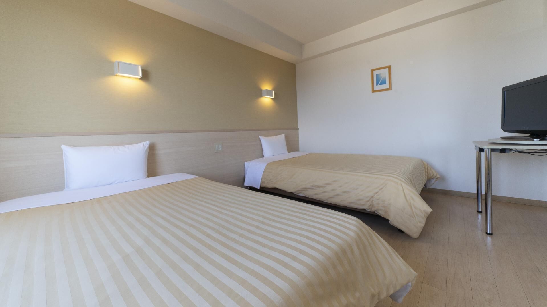 A hotel room with two beds, a television on a small table, and two wall-mounted lights.