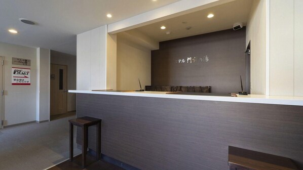 A reception area with a counter, a wall-mounted sign, and a door in the background. - Hotel Monzen No Yu (Joetsu)