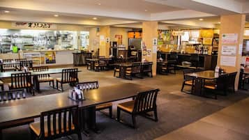 Un restaurante con varias mesas y sillas, una zona de cocina, y diferentes letreros y menús.
