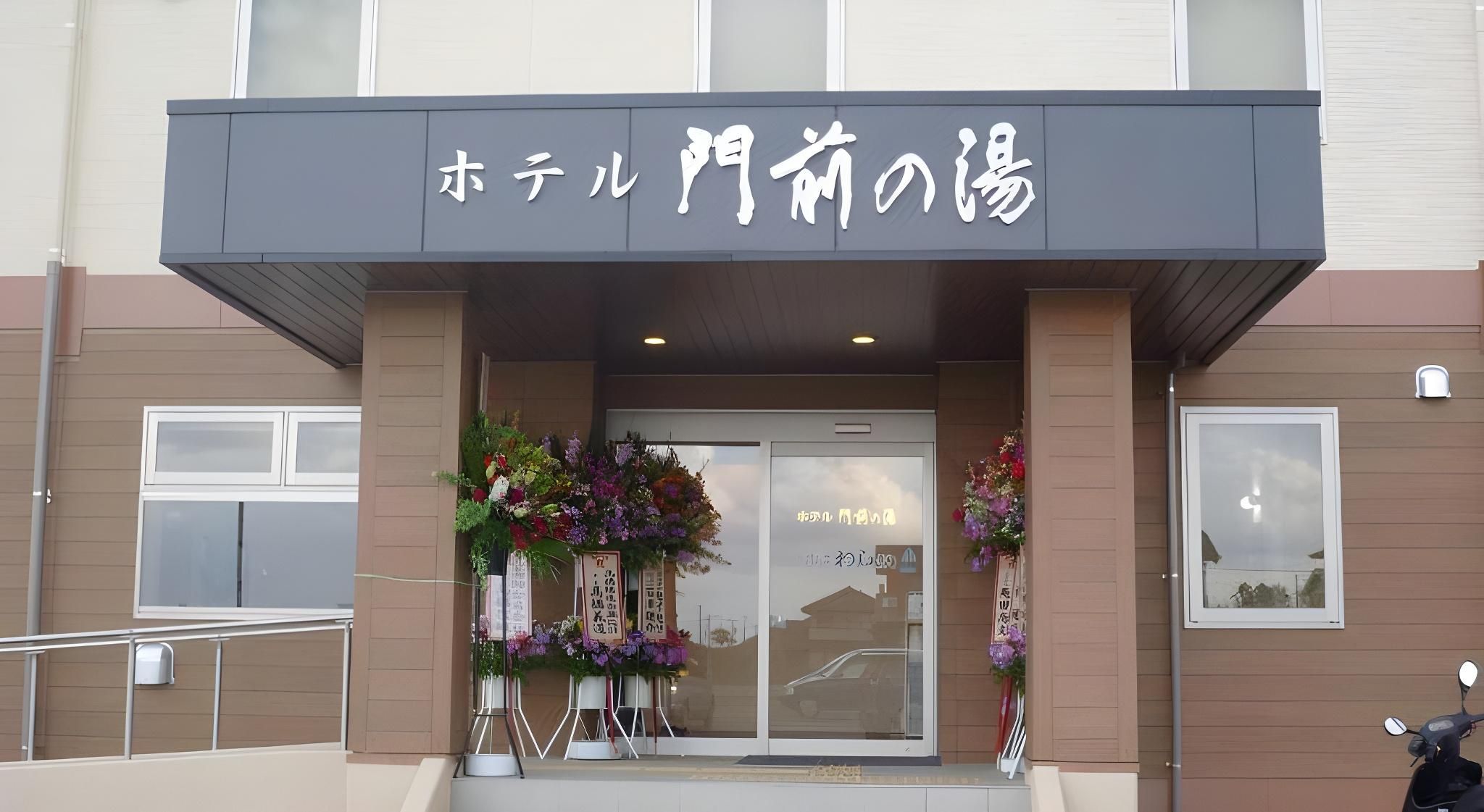 Entrada de hotel con un letrero en japonés, puerta de vidrio y decoración floral.