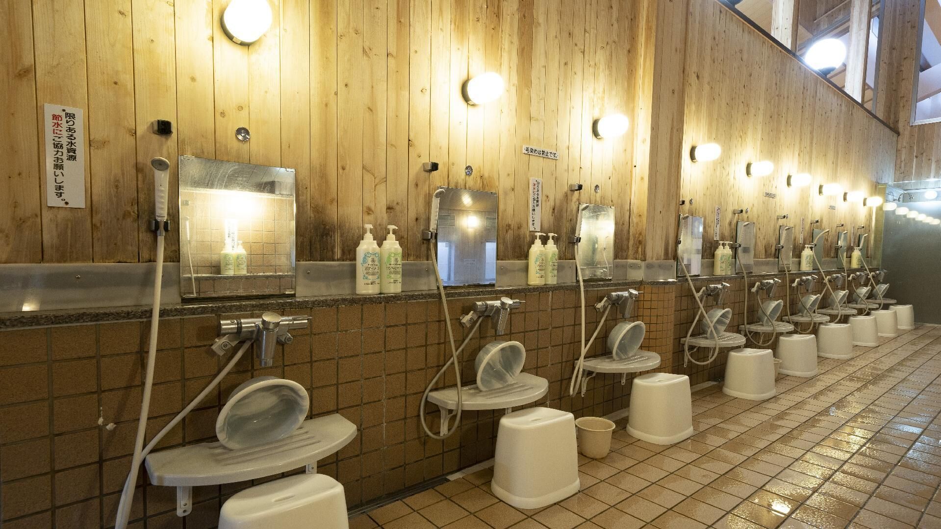 A row of public restrooms with individual sinks and toilets, wooden walls, and overhead lighting.