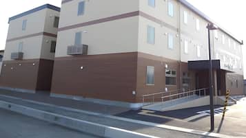 Un edificio de varios pisos con techo plano, una rampa que conduce a la entrada y una farola.