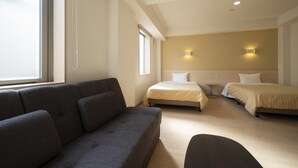 A hotel room with a sofa, two single beds, a small table, and a window. - Hotel Monzen No Yu (Joetsu)