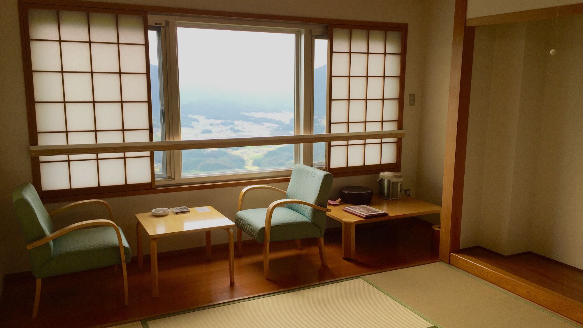 Une pièce de style japonais traditionnel, avec un sol recouvert de tatamis, une table basse, deux chaises et une vue à travers des panneaux coulissants.