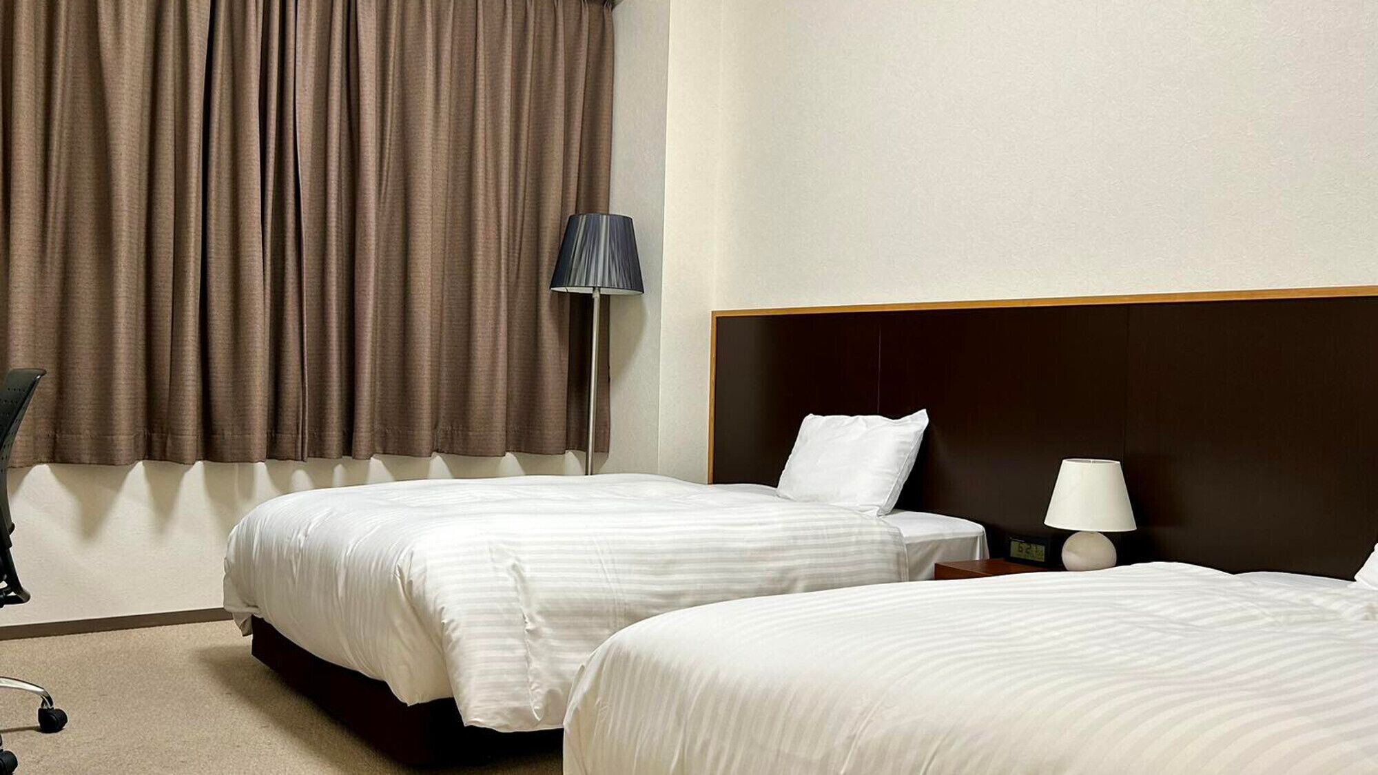 Une chambre d’hôtel avec deux lits, un bureau, une chaise et une lampe.