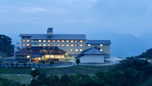 A multi-story hotel with a flat roof, a parking lot, and a small adjacent building. - Ikoinomura Shimane (Onan)