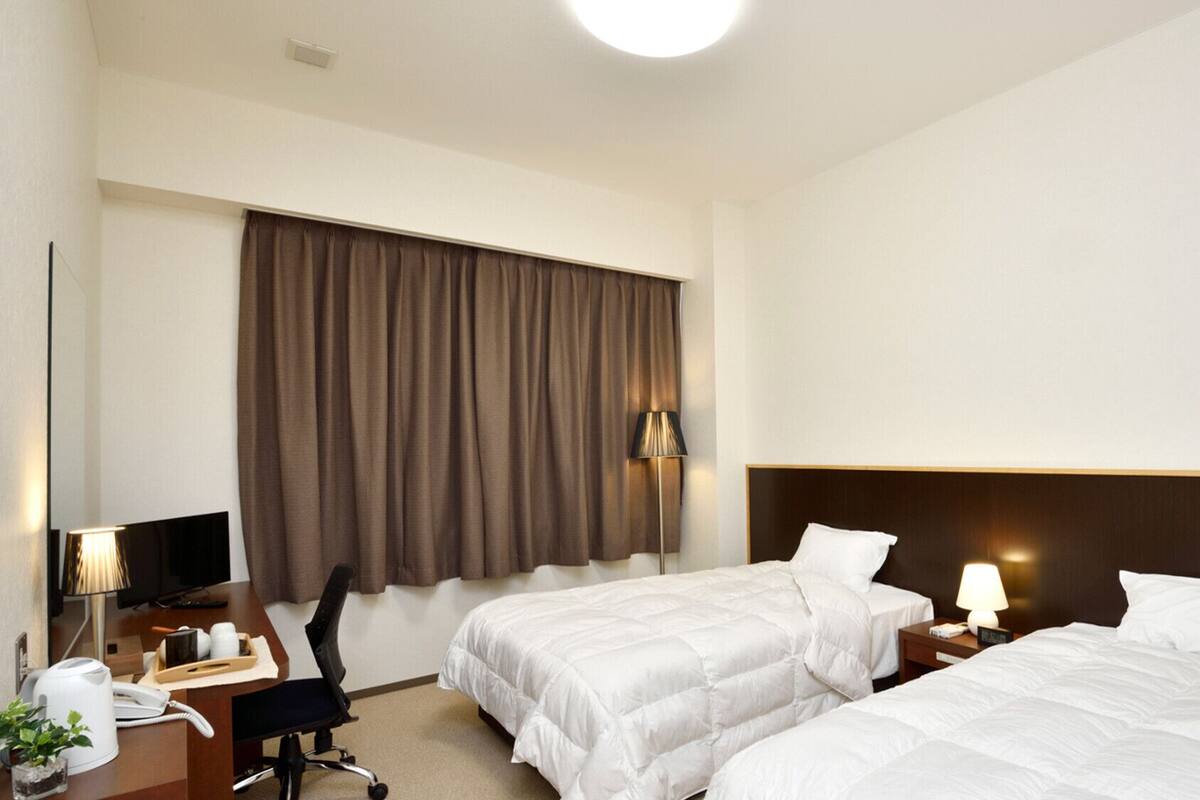 A hotel room with two beds, a desk with a telephone, a chair, a lamp, and a window with curtains.