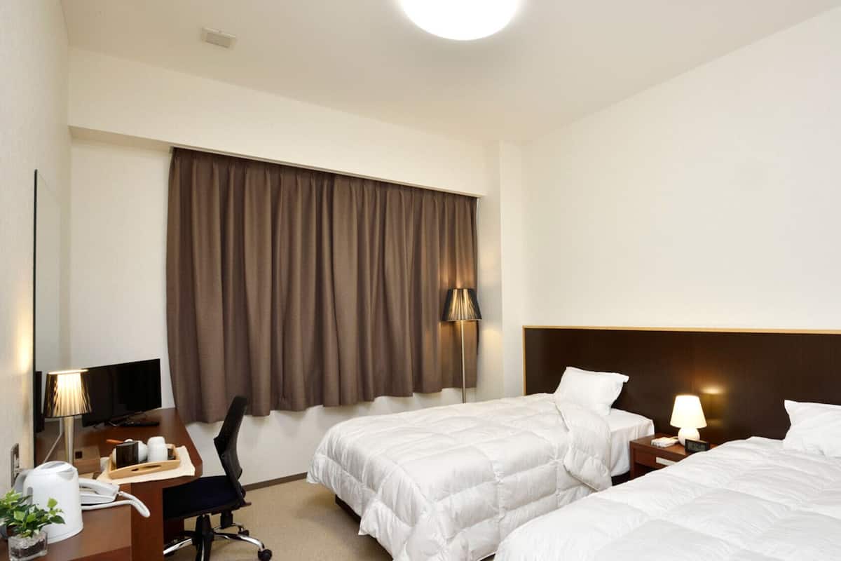 A hotel room with two beds, a desk with a telephone, a chair, a lamp, and a window with curtains.