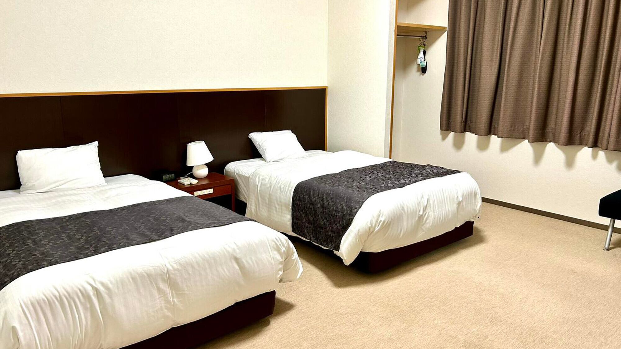 Une chambre d’hôtel avec deux lits, une table de chevet, une lampe, une armoire et une fenêtre avec des rideaux.