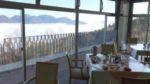 A dining area with a table set for two, chairs, and a view of mountains through large windows. - Ikoinomura Shimane (Onan)