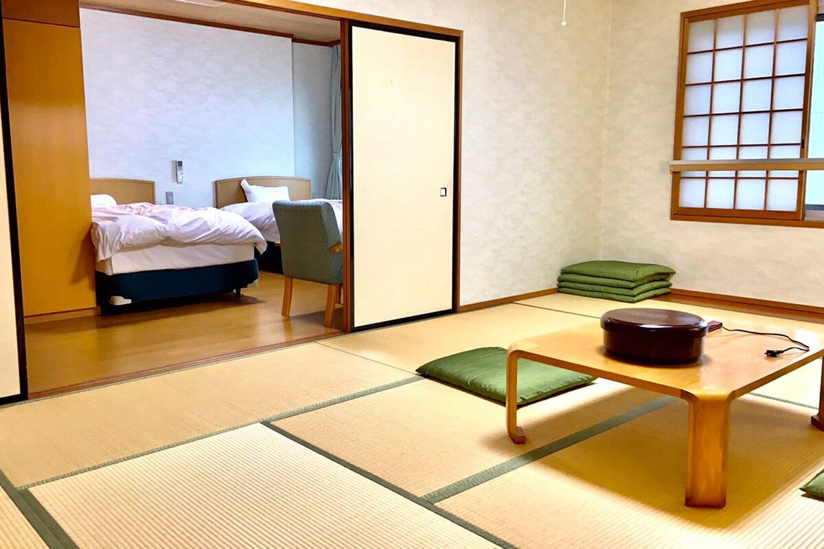 A traditional Japanese-style room with tatami flooring, a futon bed, a low table with a cushion, and a shoji screen.