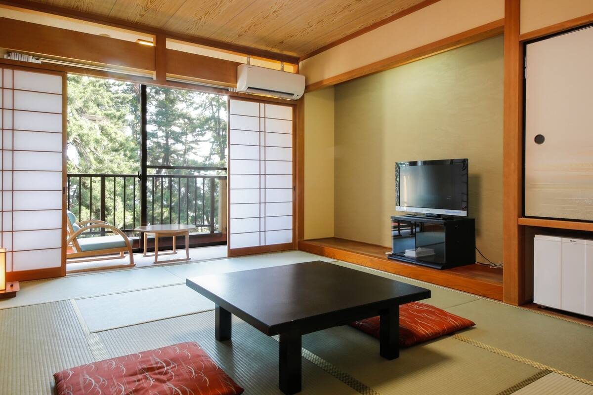 A traditional Japanese room with tatami flooring, a low table, a television, and a sliding door leading to a balcony.