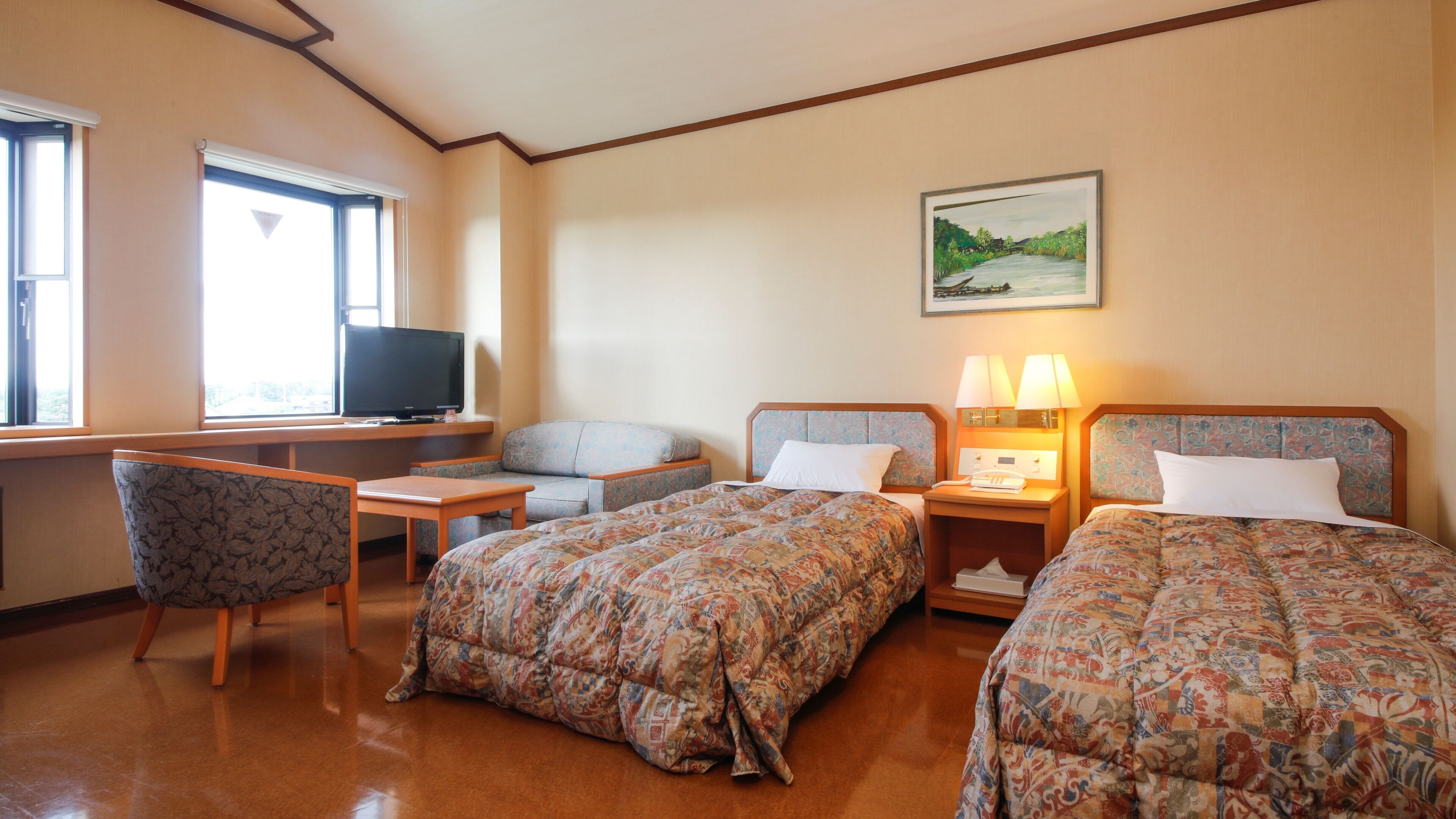 Habitación de hotel con dos camas, un escritorio con televisor, una silla y un cuadro en la pared.