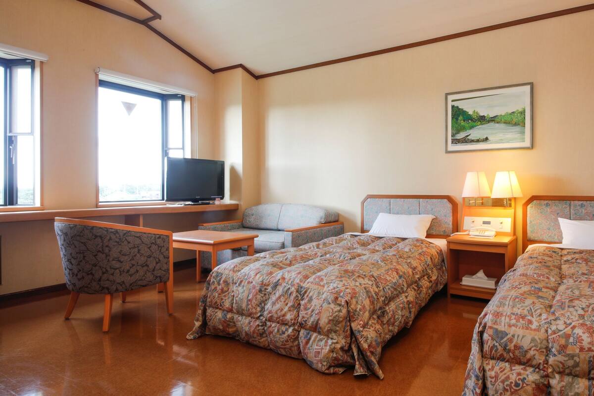 A hotel room with two beds, a desk with a TV, a chair, and a painting on the wall.