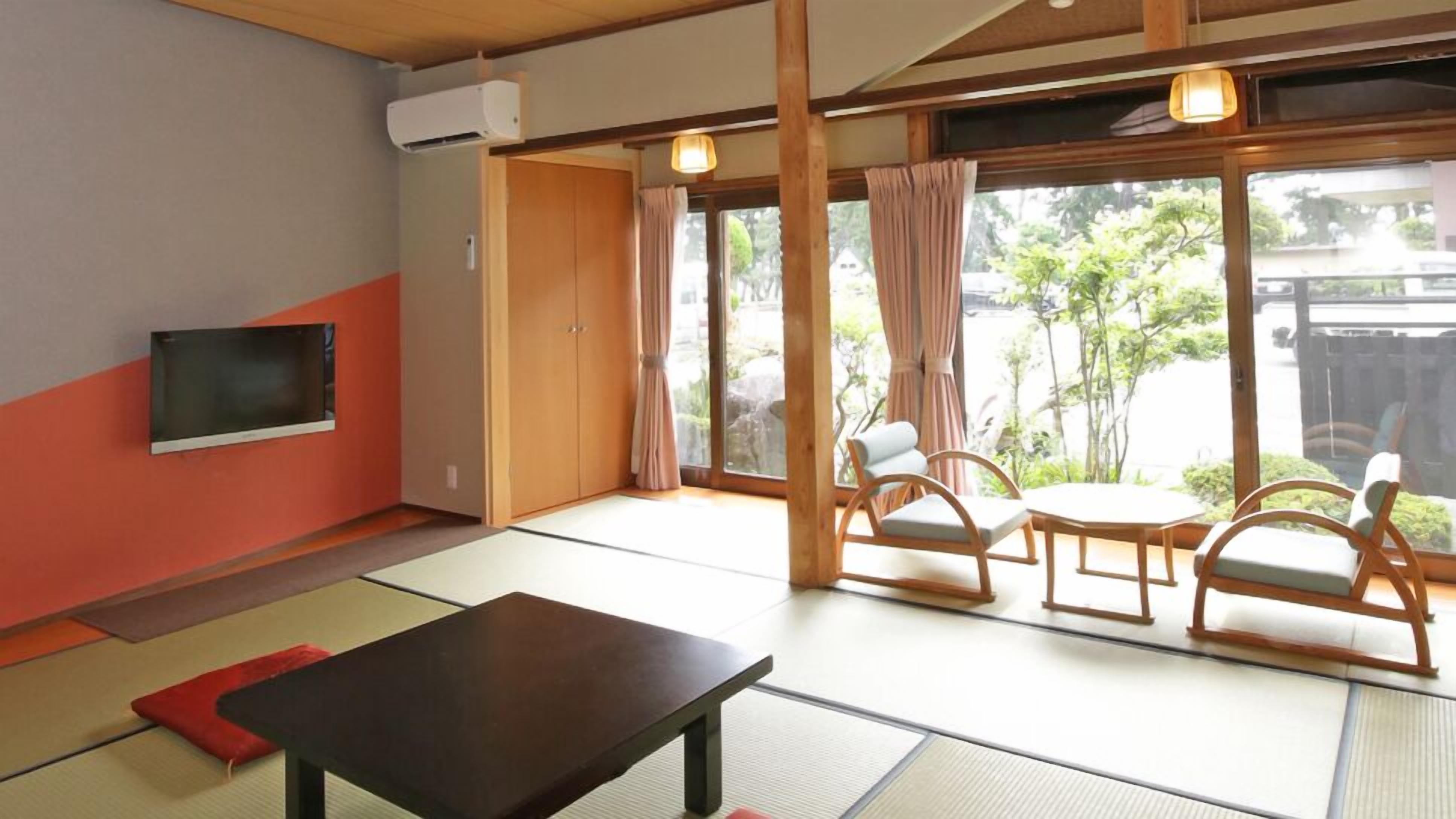 A room with tatami flooring, a television, a table, and a view of greenery outside.
