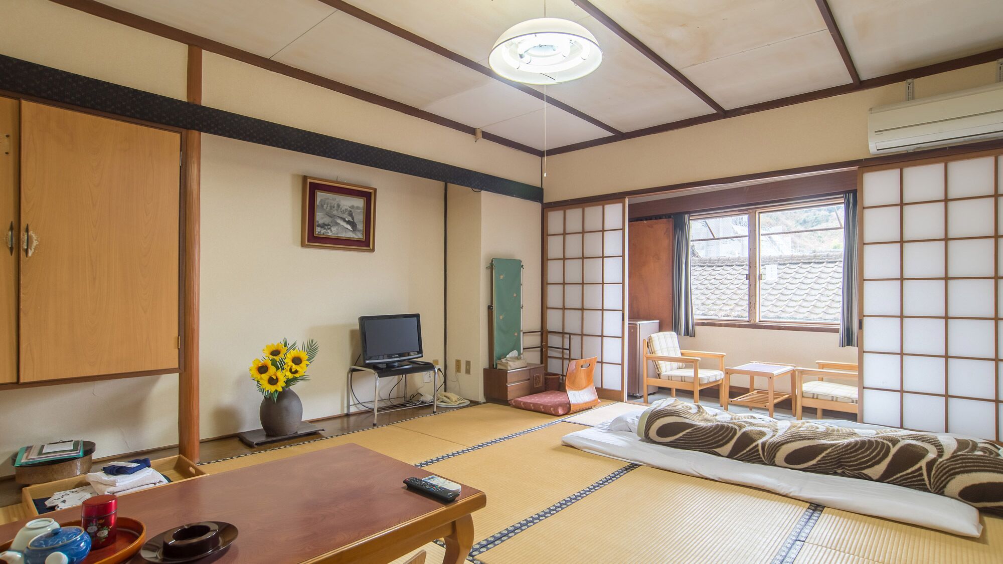 A traditional Japanese-style room with tatami flooring, a television, a desk, and a futon bed.