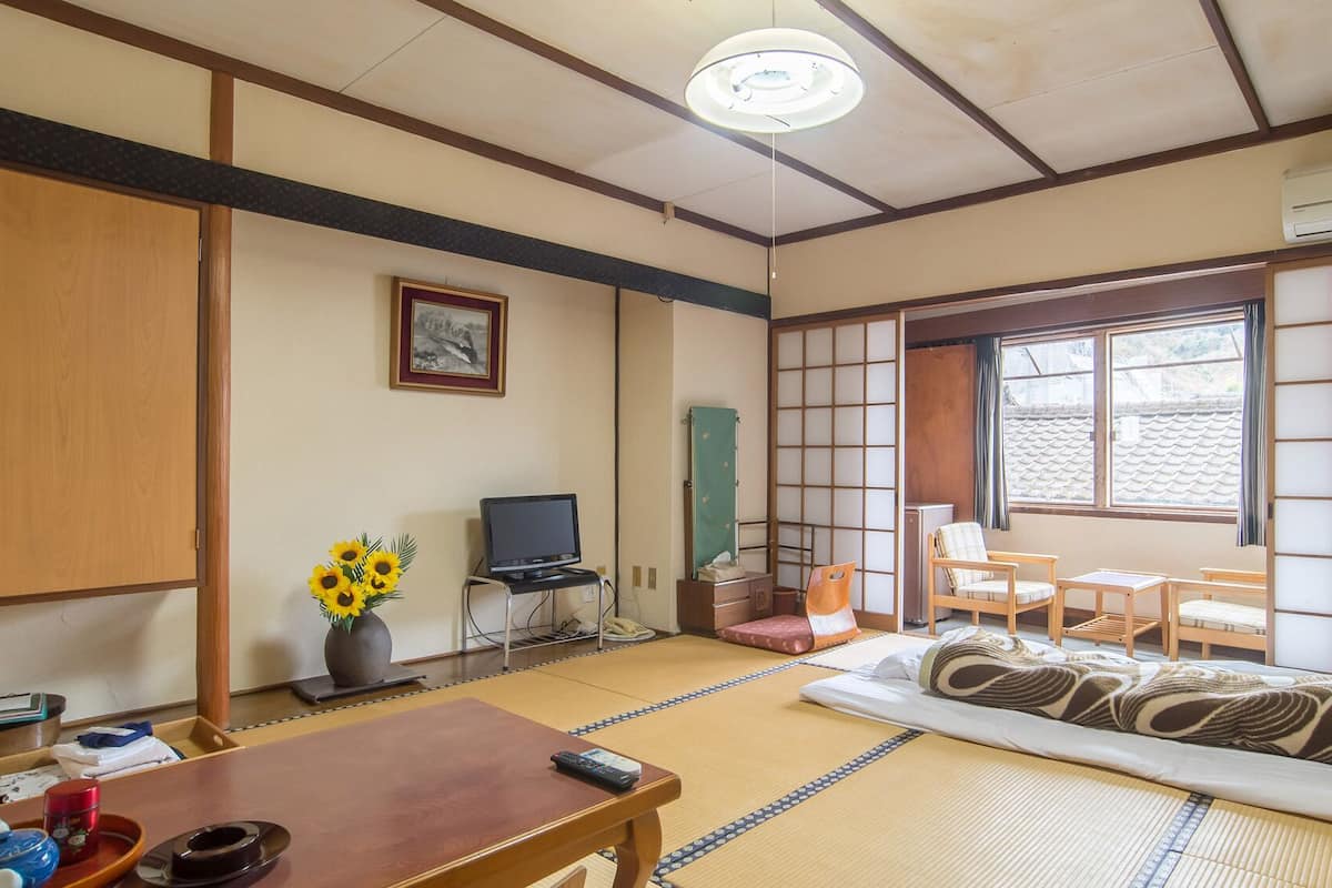 A traditional Japanese-style room with tatami flooring, a television, a desk, and a futon bed.