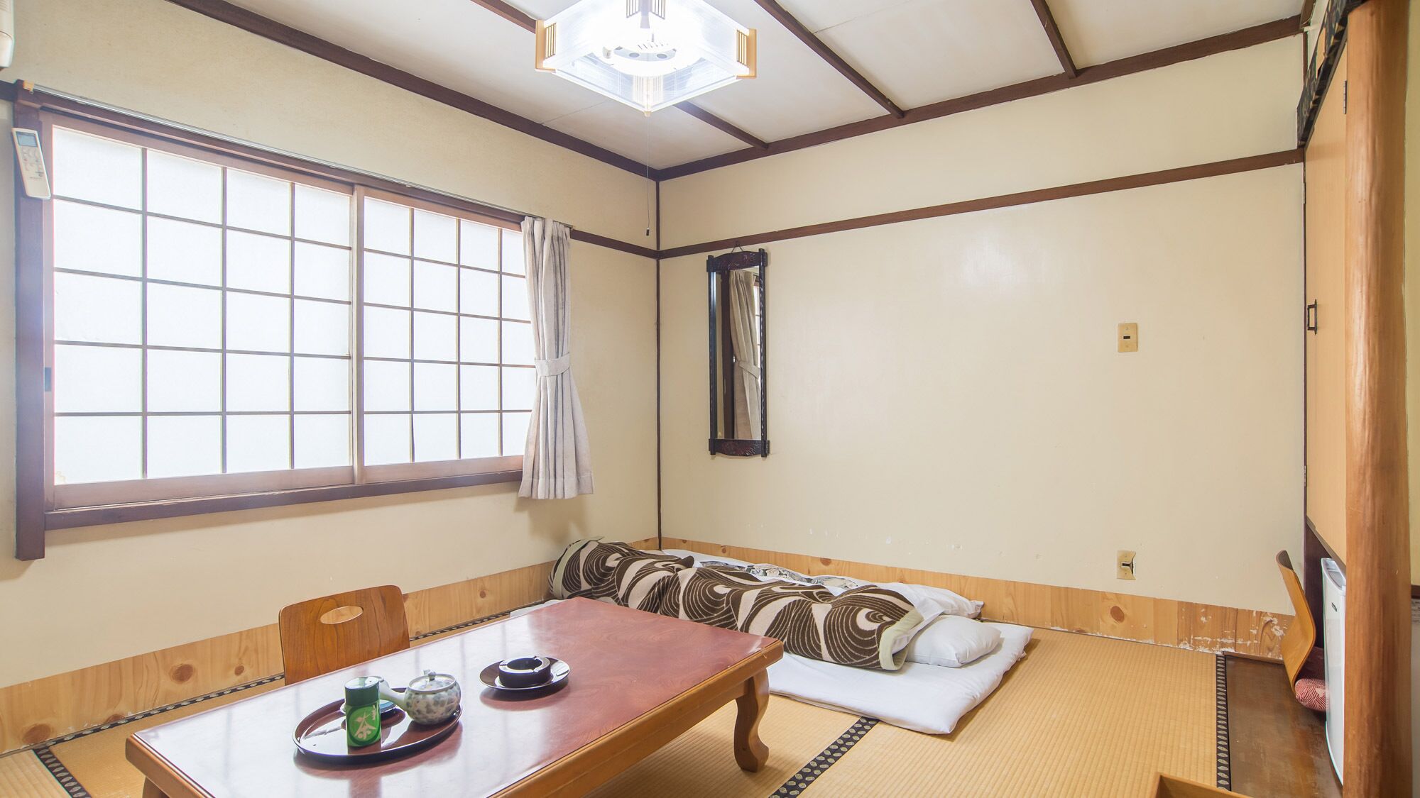 A traditional Japanese room with tatami flooring, a low wooden table with tea set, a cushioned bench, and a large window with a view.