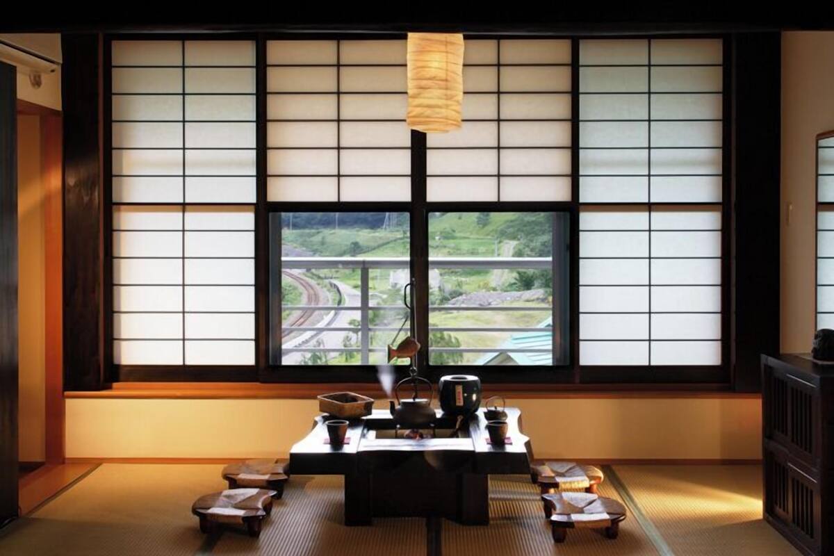 Una habitación japonesa tradicional con suelo de tatami, una mesa baja con juego de té y vista a una autopista a través de biombos shoji.
