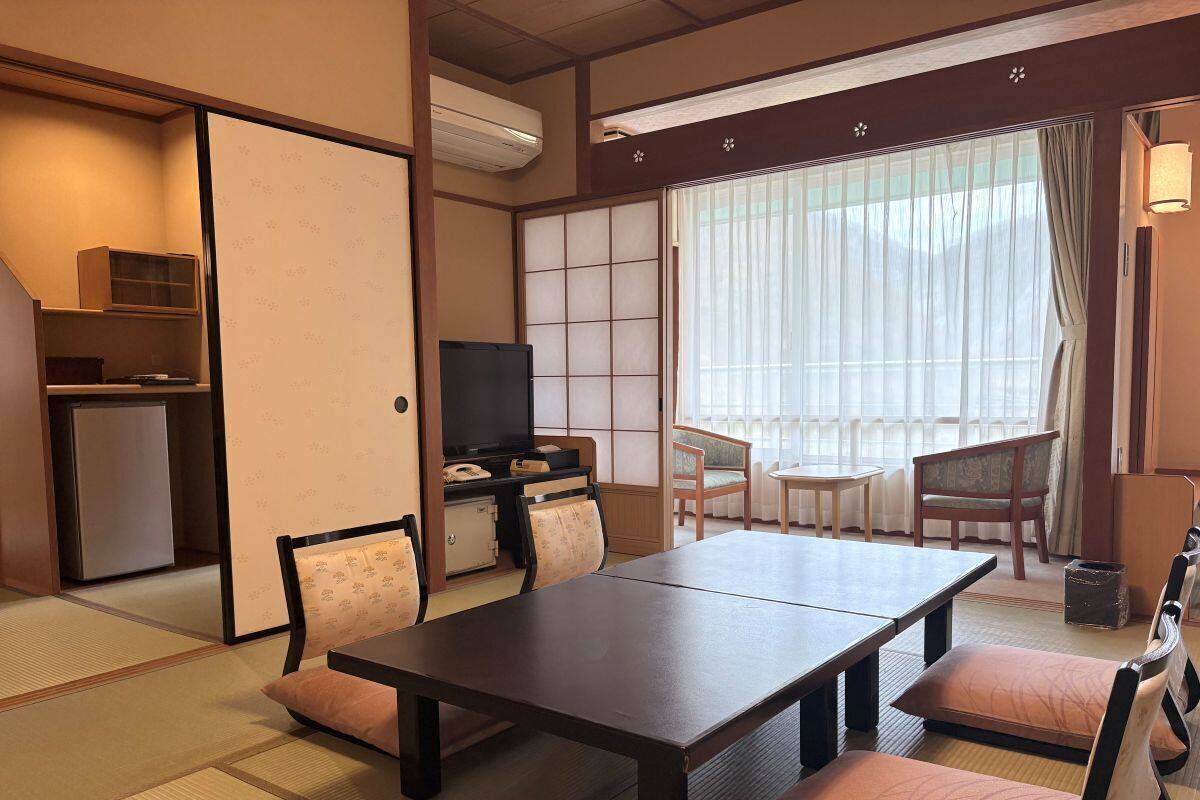 Una habitación tradicional japonesa con suelo de tatami, una mesa baja, asientos acolchados, un televisor y puertas correderas.