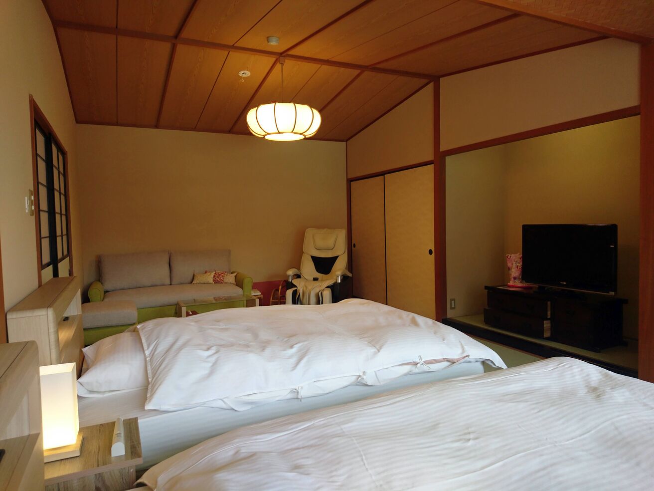 Een hotelkamer met een groot bed, een stoel, een televisietoestel en een traditioneel Japans plafond.