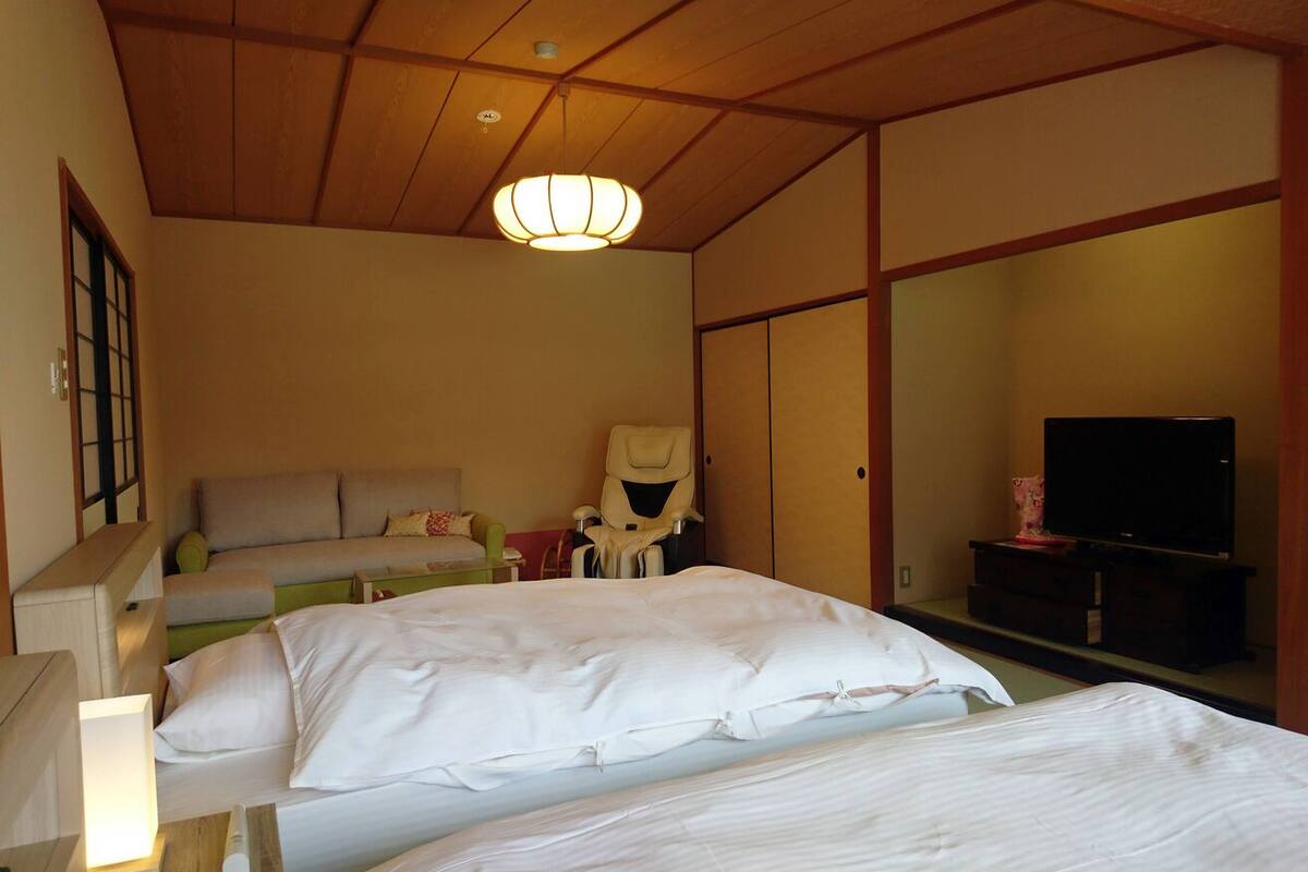 Habitación de hotel con una cama grande, una silla, un televisor y un techo al estilo tradicional japonés.