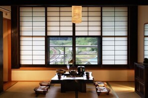 Ein traditioneller japanischer Raum mit Tatami-Böden, einem niedrigen Tisch mit Teeservice und Blick auf eine Straße durch einen Shoji-Bildschirm.