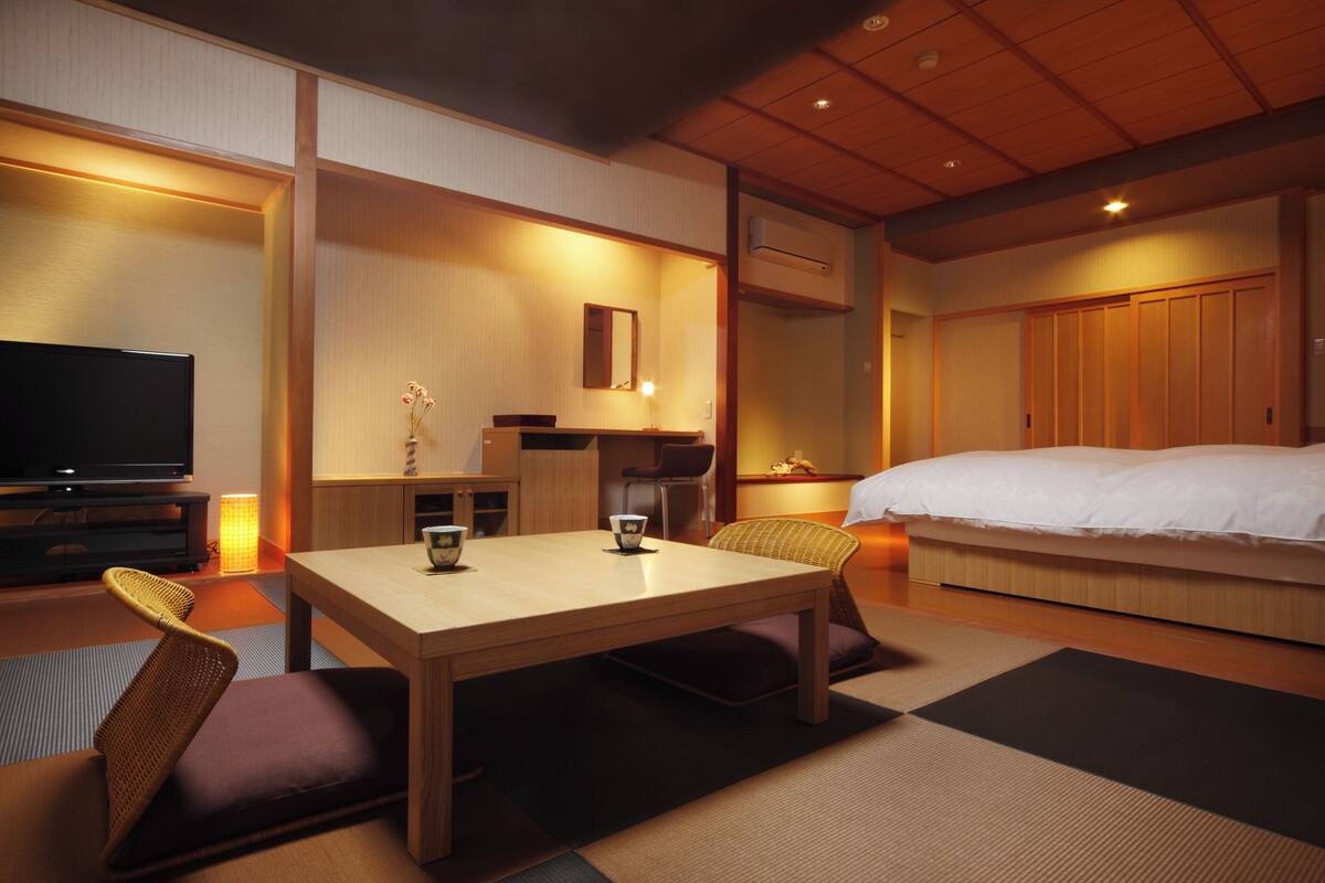 Una habitación de hotel con cama, televisión, mesa de comedor y una pequeña cocina.