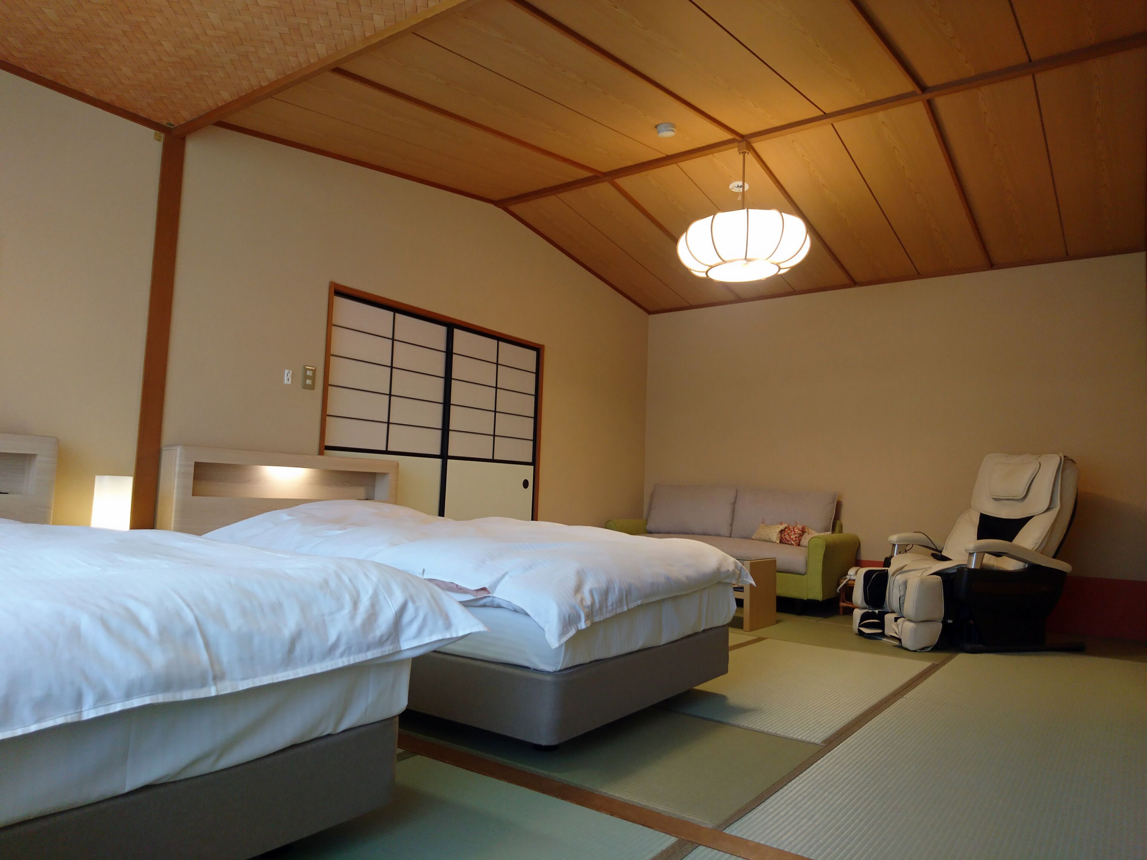 Ein traditioneller japanischer Raum mit Tatami-Boden, zwei Betten, einem Futon, einem Shoji-Bildschirm und einem Massagesessel.