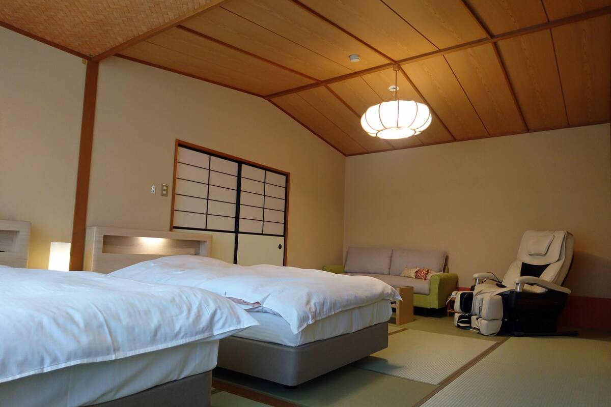 Una habitación tradicional japonesa con suelo de tatami, dos camas, un futón, un panel shoji y un sillón de masaje.