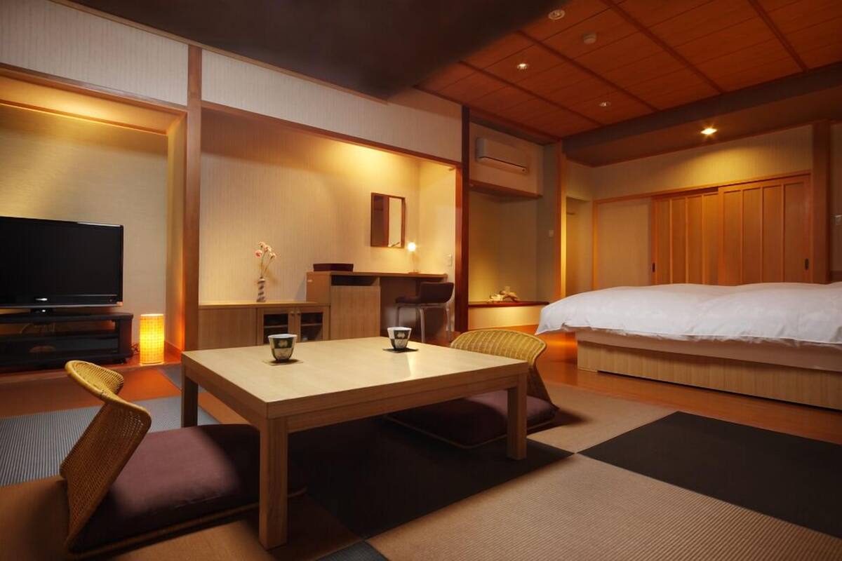 Una habitación de hotel con cama, televisión, mesa de comedor y pequeña cocina.