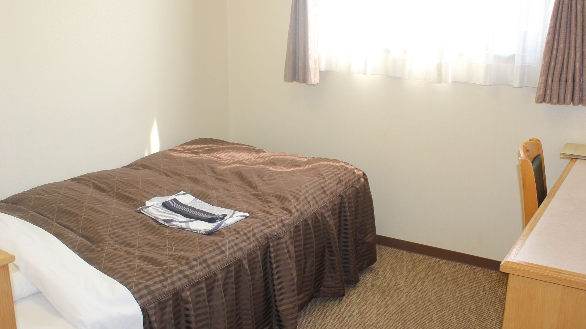 A small, neatly made room with a single bed, a desk, and a chair.