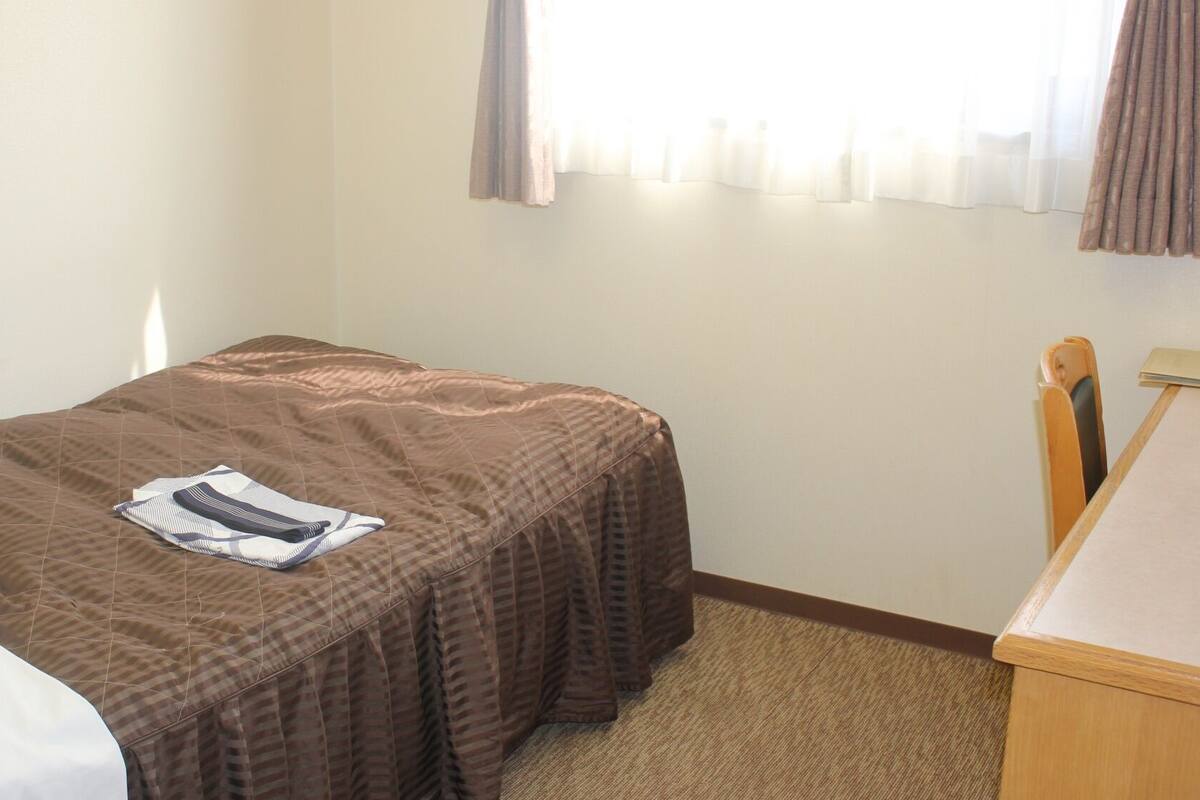 A small, neatly made room with a single bed, a desk, and a chair.