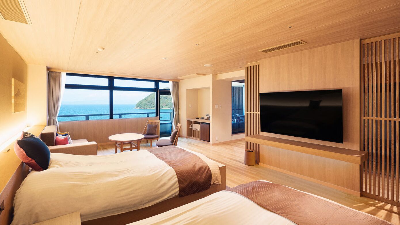 Ein modernes Hotelzimmer mit zwei Betten, einem Fernseher, einer kleinen Essecke und Meerblick.
