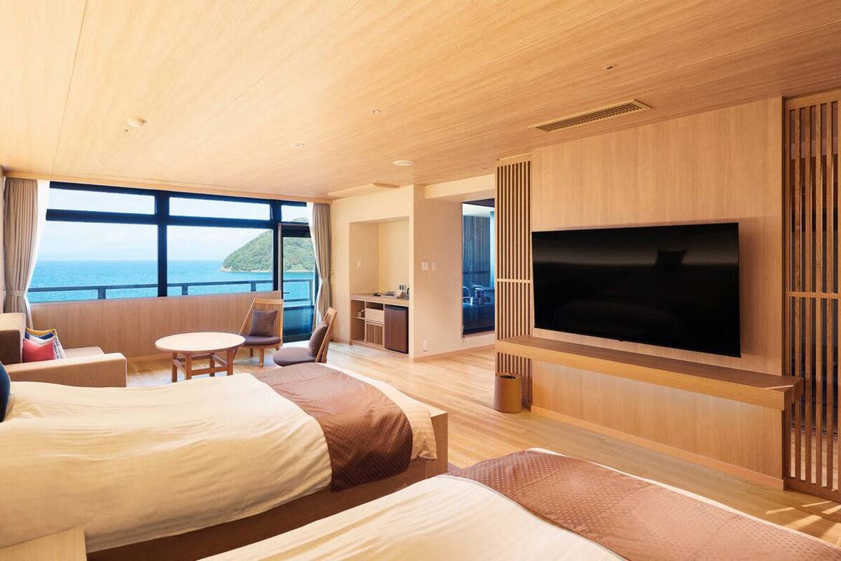 Ein modernes Hotelzimmer mit zwei Betten, einem Fernseher, einer kleinen Essecke und Meerblick.