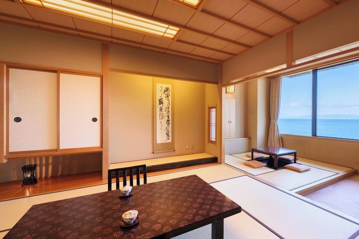 Ein traditioneller japanischer Raum mit Tatami-Böden, einem niedrigen Tisch mit einer Schüssel, einer Schiebetür und Blick aufs Meer.